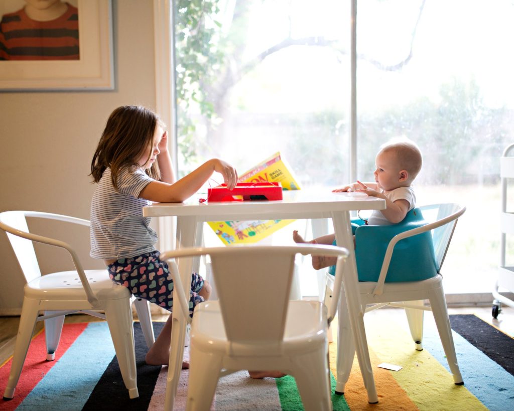 sister and baby sitting on chair and playing on table near window