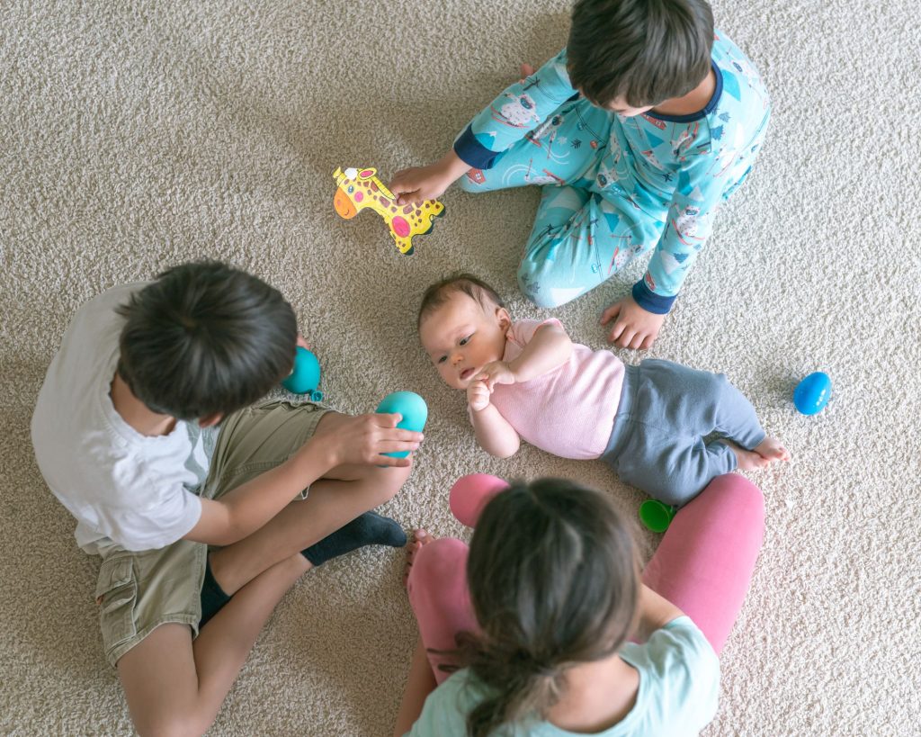 Socializing will be easier for them three kids are playing with toys and newborn baby is in their center