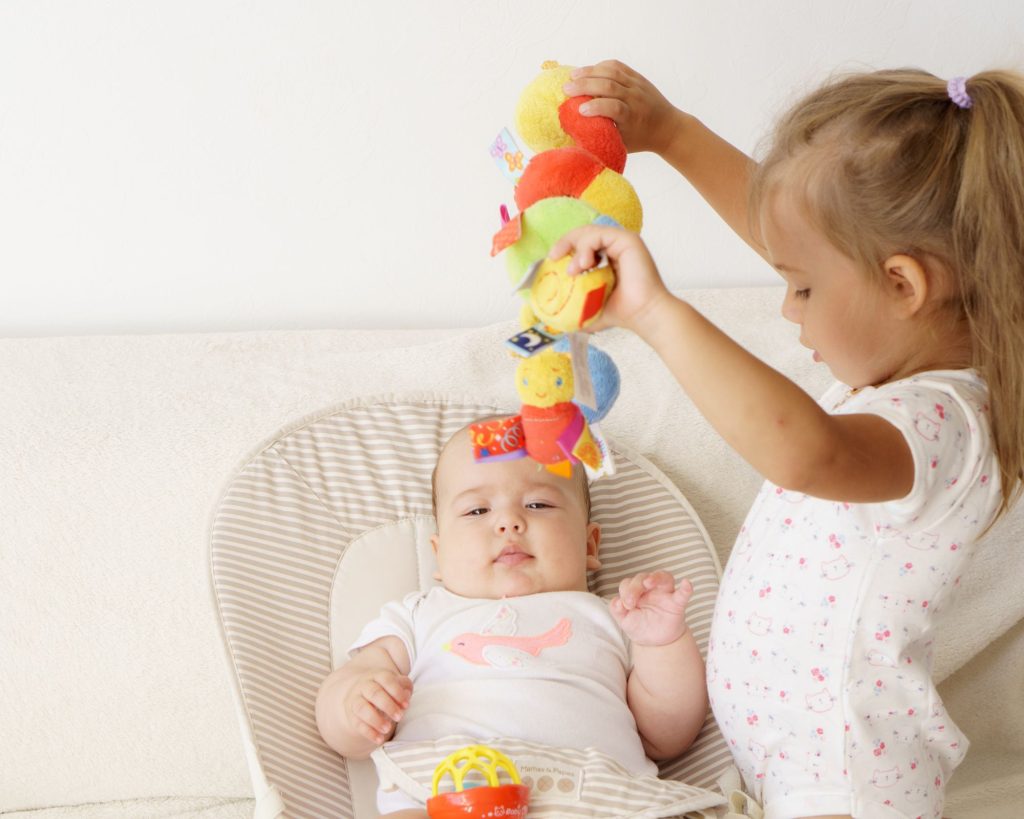 You're adding another best friend for your older children baby is laying and sister is playing with her by hanging the toys